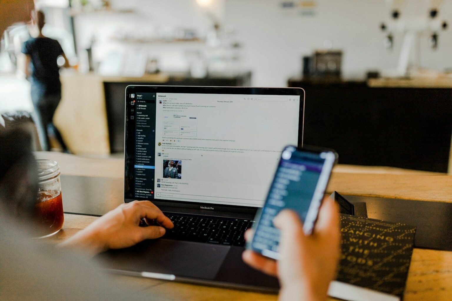 Une main tient un téléphone devant un ordinateur portable ouvert sur une table